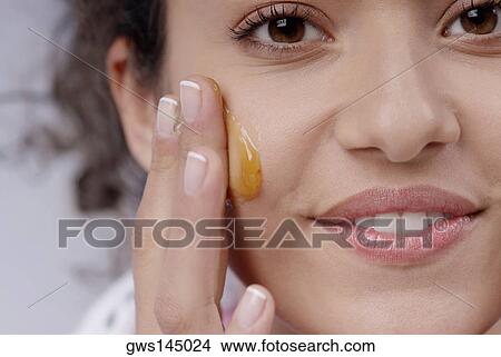 Portrait of a young woman applying honey on her cheek View Large Photo Image Picture - Portrait of a young woman applying honey on her cheek. Fotosearch
