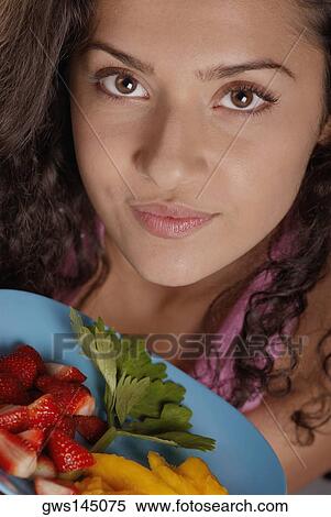 Stock Photography - Portrait of a young woman holding a plate of fruit. Fotosearch