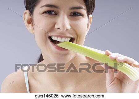 Stock Photograph - Portrait of a young woman eating a cucumber. Fotosearch