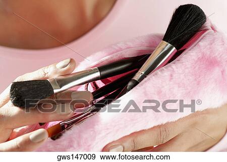 Stock Photo - Close-up of a young woman holding make-up brushes in a purse. Fotosearch