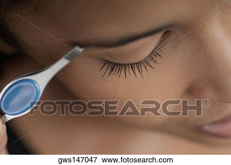 Stock Photo - Close-up of a young woman plucking her eyebrows. Fotosearch