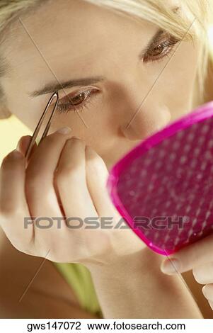 Stock Image - High angle view of a young woman tweezing her eyebrows. Fotosearch
