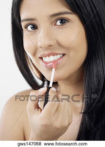 Portrait of a young woman applying lipstick View Large Photo Image Stock Photo - Portrait of a young woman applying lipstick. Fotosearch