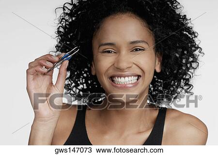Stock Image - Portrait of a young woman holding a pair of eyebrow tweezers. Fotosearch