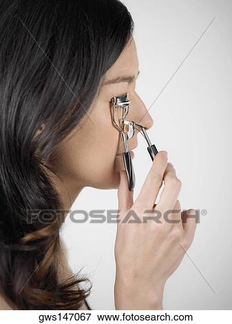 Stock Photo - Side profile of a young woman using an eyelash curler. Fotosearch