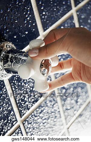 Picture - Close-up of a human hand turning a shower knob. Fotosearch