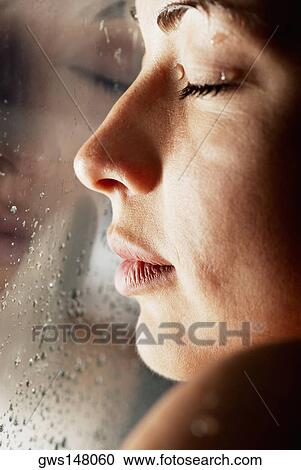 Stock Image - Close-up of a young woman with her face against a glass window. Fotosearch