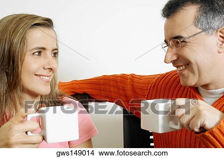 Close-up of a mid adult couple holding two cups of coffee View Large Photo Image Picture - Close-up of a mid adult couple holding two cups of coffee. Fotosearch