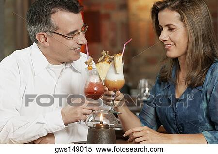 Stock Photography - Close-up of a mid adult couple sitting in a restaurant and toasting glasses of pina colada. Fotosearch