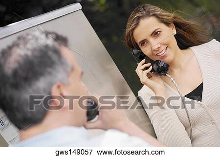 Stock Photo - Close-up of a mid adult couple talking on a pay phone. Fotosearch