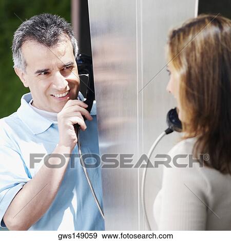 Close-up of a mid adult couple talking on a pay phone View Large Photo Image Stock Photo - Close-up of a mid adult couple talking on a pay phone. Fotosearch