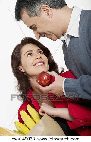 Close-up of a mid adult man holding an apple with a mid adult woman holding a shopping bag beside her View Large Photo Image Stock Image - Close-up of a mid adult man holding an apple with a mid adult woman holding a shopping bag beside her. Fotosearch