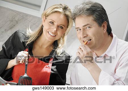 Close-up of a mid adult woman cooking food with a mature man eating food in the kitchen View Large Photo Image Stock Image - Close-up of a mid adult woman cooking food with a mature man eating food in the kitchen. Fotosearch
