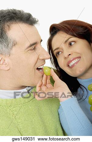 Stock Image - Close-up of a mid adult woman feeding a grape to a mid adult man. Fotosearch