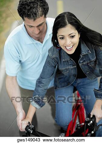 Stock Image - High angle view of a mid adult man helping a mid adult woman ride a bicycle. Fotosearch