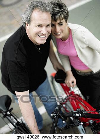 Stock Photograph - Portrait of a mature couple standing with bicycles and smiling. Fotosearch