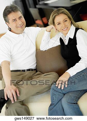 Portrait of a mature man and a mid adult woman sitting on a couch and smiling View Large Photo Image Stock Photo - Portrait of a mature man and a mid adult woman sitting on a couch and smiling. Fotosearch