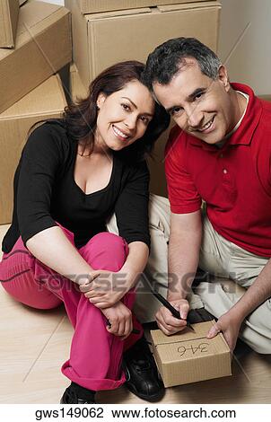 Portrait of a mid adult man writing on a cardboard box with a mid adult woman sitting beside him View Large Photo Image Stock Image - Portrait of a mid adult man writing on a cardboard box with a mid adult woman sitting beside him. Fotosearch