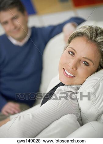 Portrait of a mid adult woman sitting on a couch and smiling and a mature man sitting in background View Large Photo Image Stock Photo - Portrait of a mid adult woman sitting on a couch and smiling and a mature man sitting in background. Fotosearch