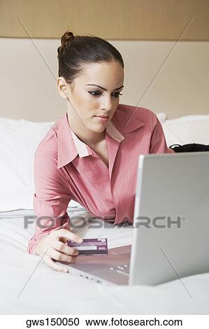 Stock Image - Close-up of a businesswoman holding a credit card and using a laptop on the bed. Fotosearch