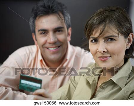 Stock Photograph - Close-up of a mature man and a mid adult woman smiling and holding a credit card. Fotosearch