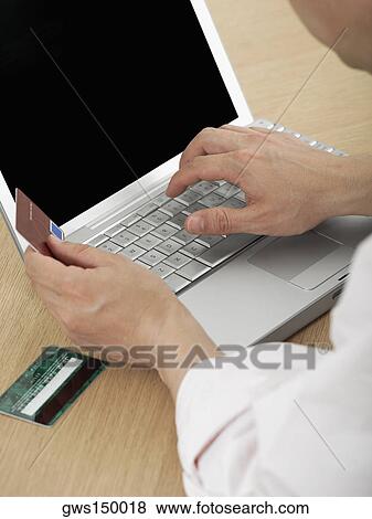 Stock Photo - Close-up of a mature man's hand holding a credit card and using a laptop. Fotosearch