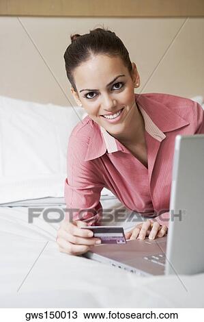 Stock Image - Portrait of a young woman holding a credit card and using a laptop. Fotosearch