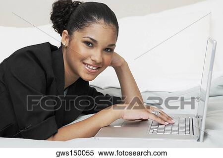 Stock Photography - Portrait of a young woman using a laptop on the bed. Fotosearch