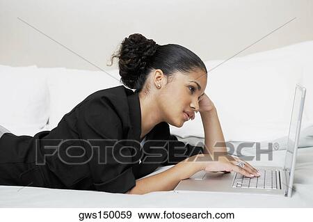 Stock Photo - Side profile of a young woman using a laptop on the bed. Fotosearch
