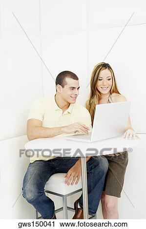 Young man using a laptop with a young woman standing near him View Large Photo Image Stock Image - Young man using a laptop with a young woman standing near him. Fotosearch