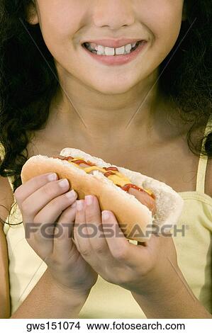 Close-up of a girl holding a hot dog and smiling View Large Photo Image Picture - Close-up of a girl holding a hot dog and smiling. Fotosearch