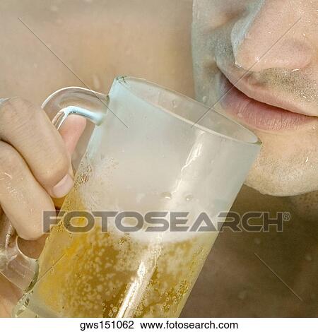 Stock Image - Close-up of a young man drinking a glass of beer. Fotosearch