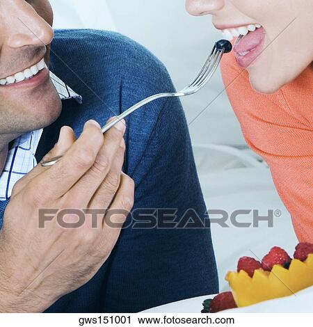 Stock Image - Close-up of a young man feeding fruit salad to a young woman. Fotosearch