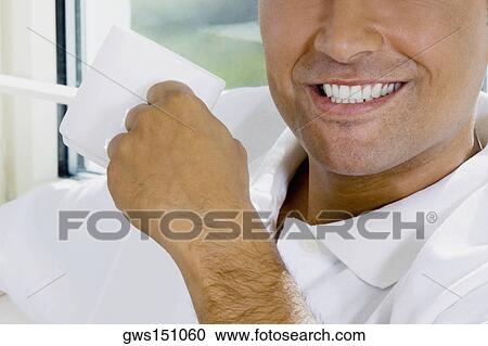 Close-up of a young man holding a cup of coffee and smiling View Large Photo Image Stock Image - Close-up of a young man holding a cup of coffee and smiling. Fotosearch