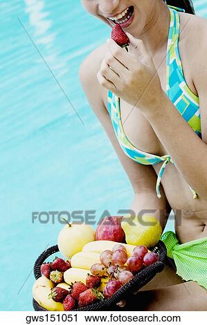 Stock Image - Close-up of a young woman eating fruit at the poolside. Fotosearch