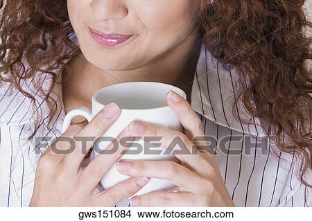 Close-up of a young woman holding a cup of coffee and smiling View Large Photo Image Picture - Close-up of a young woman holding a cup of coffee and smiling. Fotosearch