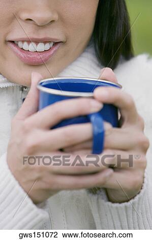 Close-up of a young woman holding a cup of coffee and smiling View Large Photo Image Stock Image - Close-up of a young woman holding a cup of coffee and smiling. Fotosearch