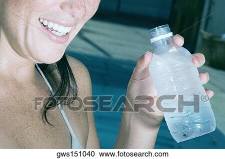 Close-up of a young woman holding a bottle of water and smiling View Large Photo Image Stock Image - Close-up of a young woman holding a bottle of water and smiling. Fotosearch