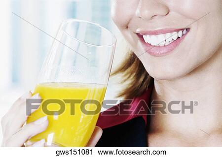Close-up of a young woman holding a glass of orange juice and smiling View Large Photo Image Stock Image - Close-up of a young woman holding a glass of orange juice and smiling. Fotosearch