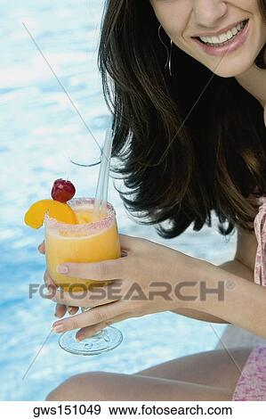 Close-up of a young woman holding a glass of orange juice at the poolside View Large Photo Image Stock Photo - Close-up of a young woman holding a glass of orange juice at the poolside. Fotosearch