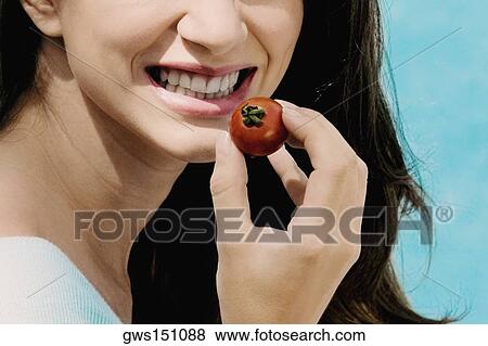 Stock Photo - Close-up of a young woman holding a cherry tomato and smiling. Fotosearch