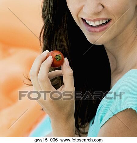 Close-up of a young woman holding a cherry tomato and smiling View Large Photo Image Stock Photograph - Close-up of a young woman holding a cherry tomato and smiling. Fotosearch
