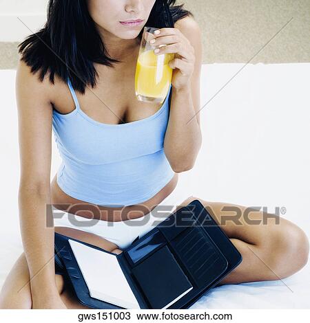 Close-up of a young woman sitting on the bed and holding a glass of orange juice View Large Photo Image Stock Image - Close-up of a young woman sitting on the bed and holding a glass of orange juice. Fotosearch