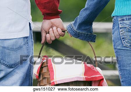 Stock Photo - Mid section view of a man and a woman carrying a wicker basket. Fotosearch