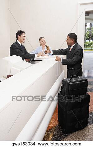 Picture - Businessman and two receptionists at a hotel reception. Fotosearch