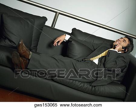 Stock Photography - Businessman reclining on a couch and talking on a mobile phone. Fotosearch