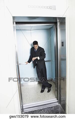 Businessman standing in an elevator and looking at his wristwatch View Large Photo Image Stock Photo - Businessman standing in an elevator and looking at his wristwatch. Fotosearch