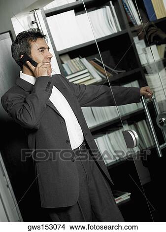 Close-up of a businessman opening a glass door and talking on a mobile phone View Large Photo Image Picture - Close-up of a businessman opening a glass door and talking on a mobile phone. Fotosearch
