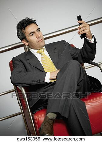 Close-up of a businessman sitting and looking at a mobile phone View Large Photo Image Stock Photograph - Close-up of a businessman sitting and looking at a mobile phone. Fotosearch