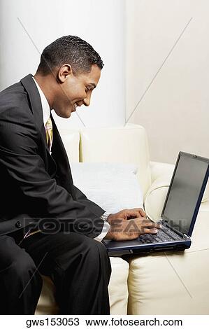 Stock Image - Close-up of a businessman using a laptop on a couch. Fotosearch